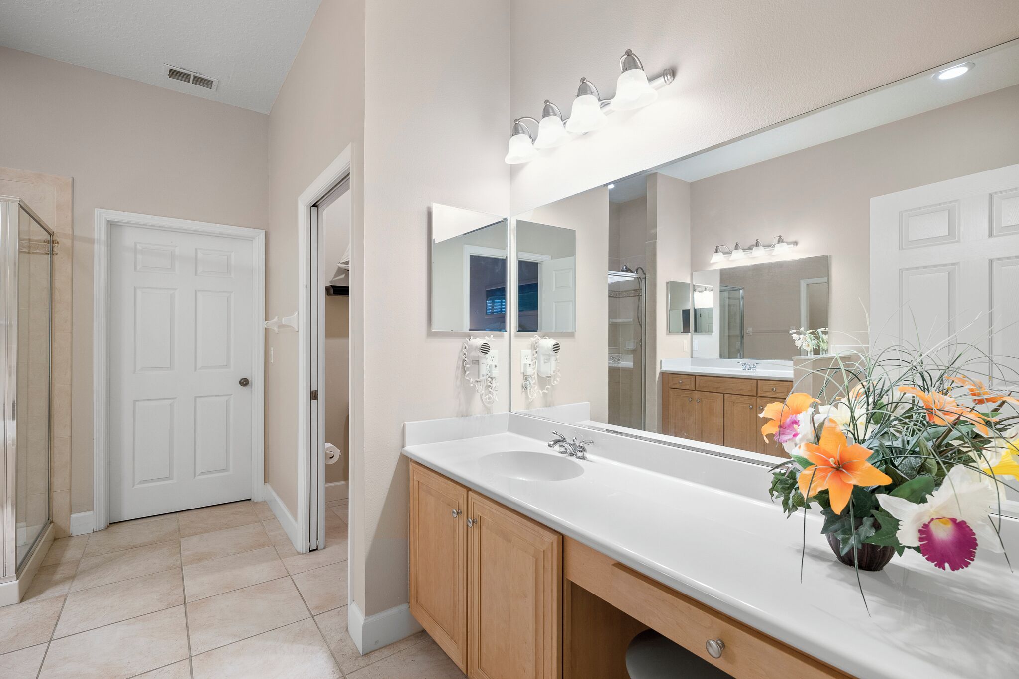 A bathroom with a white sink, wooden cabinets, a large mirror, and a flower arrangement.