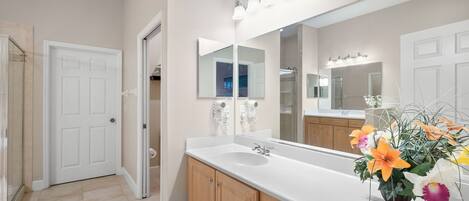 A bathroom with a white sink, wooden cabinets, a large mirror, and a flower arrangement.