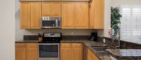 A kitchen with wooden cabinets, a stainless steel oven, a microwave, granite countertops, and a sink.