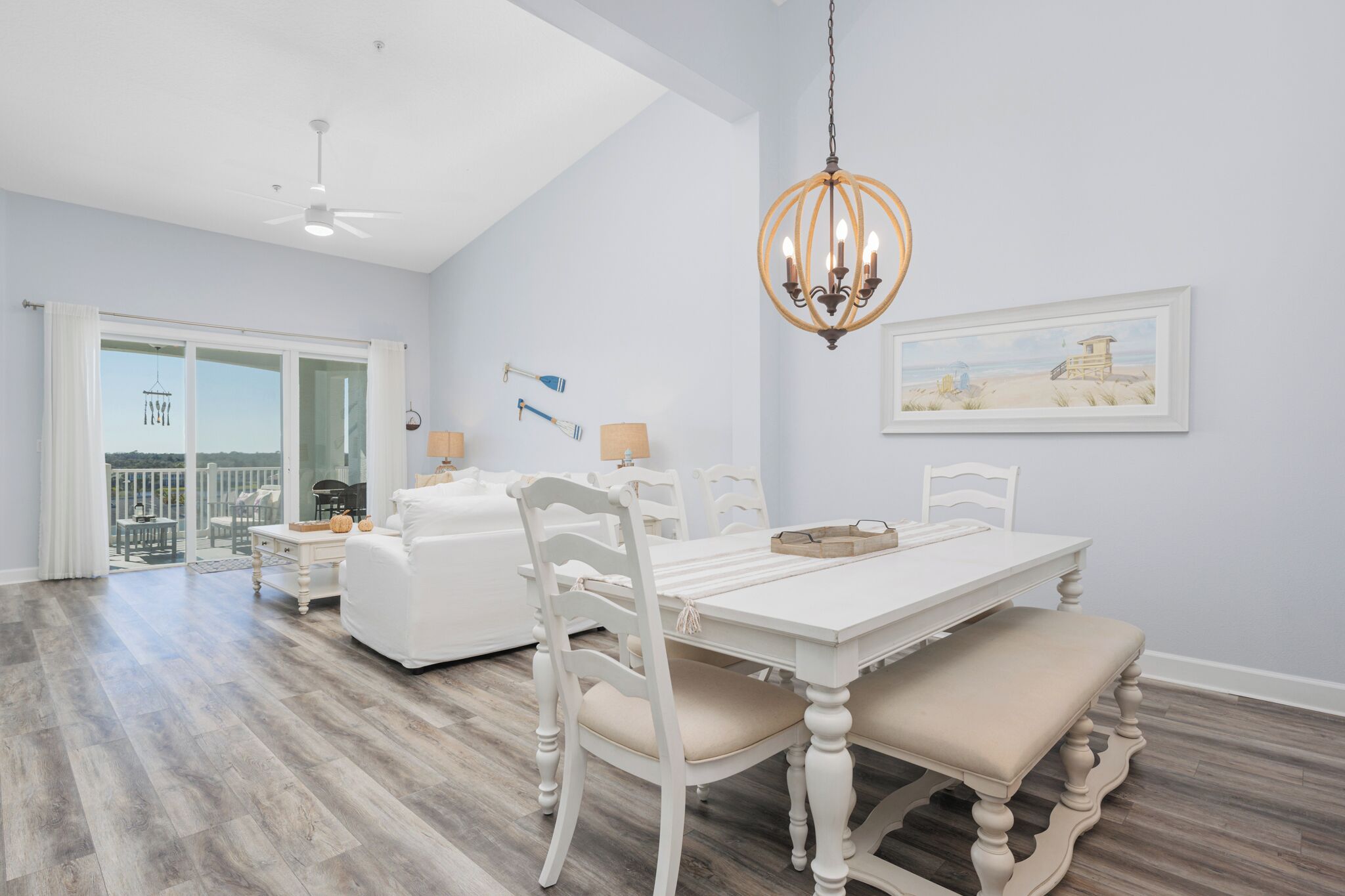A spacious dining area with a white table and chairs, a chandelier, and a framed picture on the wall.