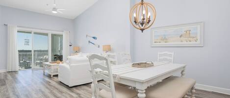 A spacious dining area with a white table and chairs, a chandelier, and a framed picture on the wall.