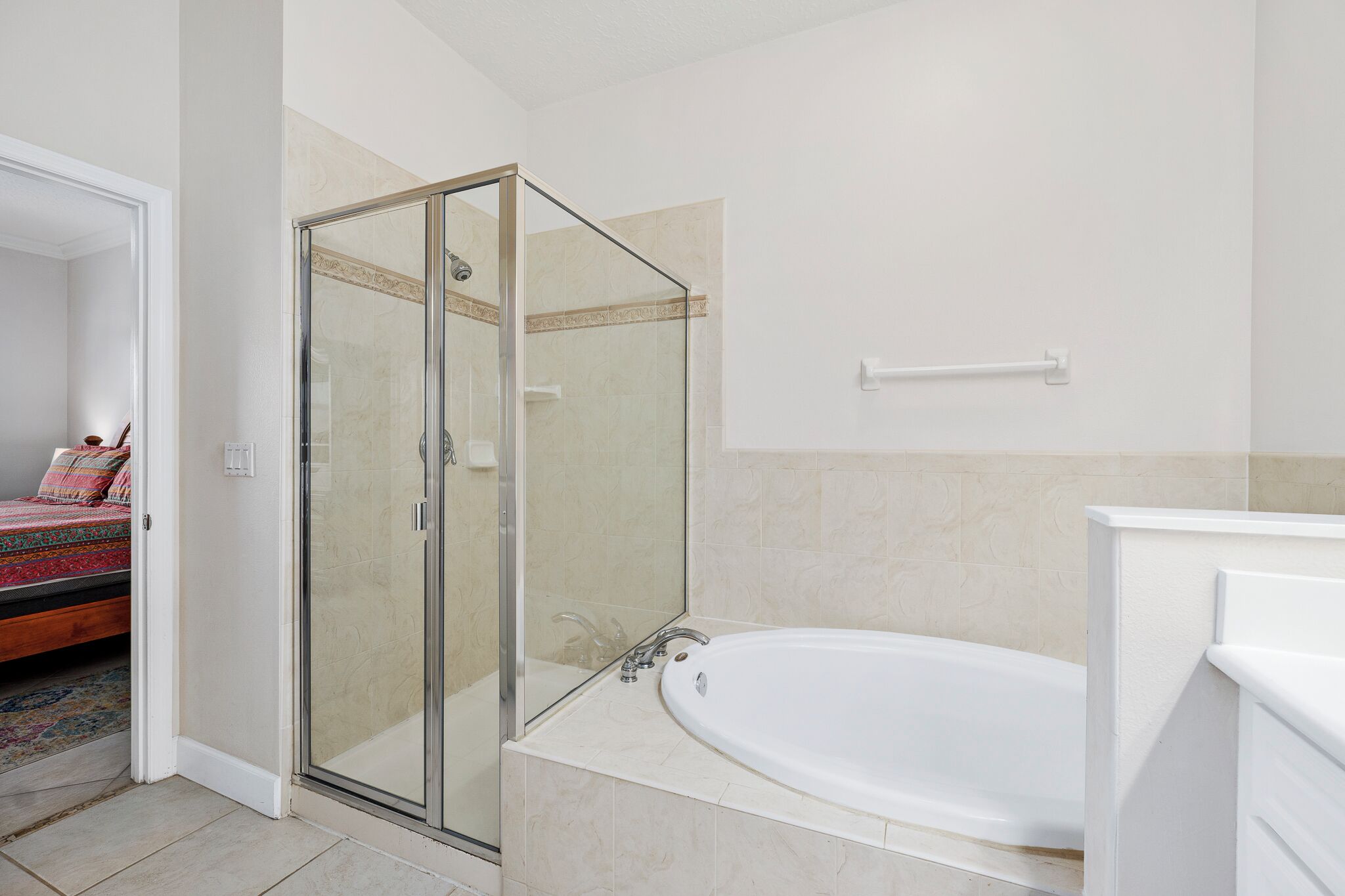 Une salle de bain moderne dotée d’une douche à parois de verre, d’une baignoire sur pieds et d’un lit visible dans la pièce adjacente, agrémenté d’une couverture colorée.