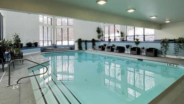 An indoor swimming pool with clear lane markings, a pool ladder, and potted plants around the perimeter. - Killington Sun Dog Trail ski-on ski-off 2 bedroom 2 bathroom 1st floor condo (Killington)