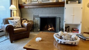 A cozy living room with a fireplace, a leather armchair, a coffee table, and a bookshelf. - Killington Sun Dog Trail ski-on ski-off 2 bedroom 2 bathroom 1st floor condo (Killington)