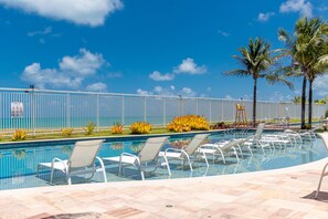 Un espace piscine agrémenté de chaises longues, de palmiers et d’un ciel d’un bleu éclatant.