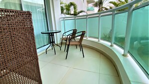 Un balcon avec un fauteuil en osier, une petite table ronde et une vue sur les palmiers et les immeubles.