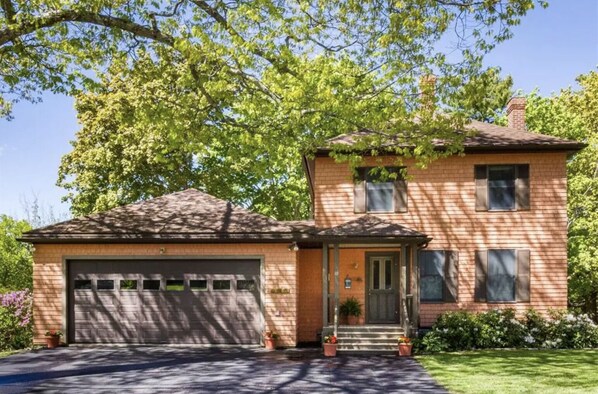 A two-story house with a garage, a front porch with potted plants, and a well-maintained lawn.