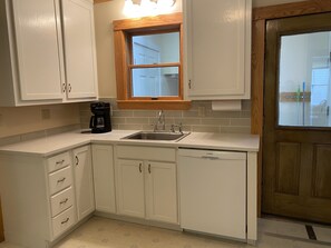 A kitchen with white cabinets, a Bosch dishwasher, a double sink, and a window above the sink.