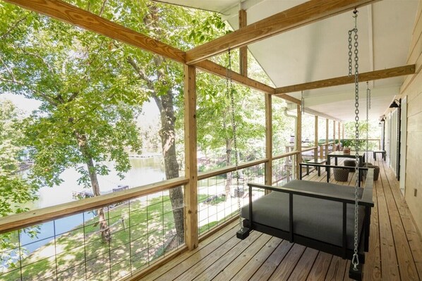 A wooden deck with a swing, a glass railing, and a view of a lake.