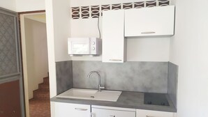 Een kleine keuken met een spoelbak, een magnetron en witte kastjes.