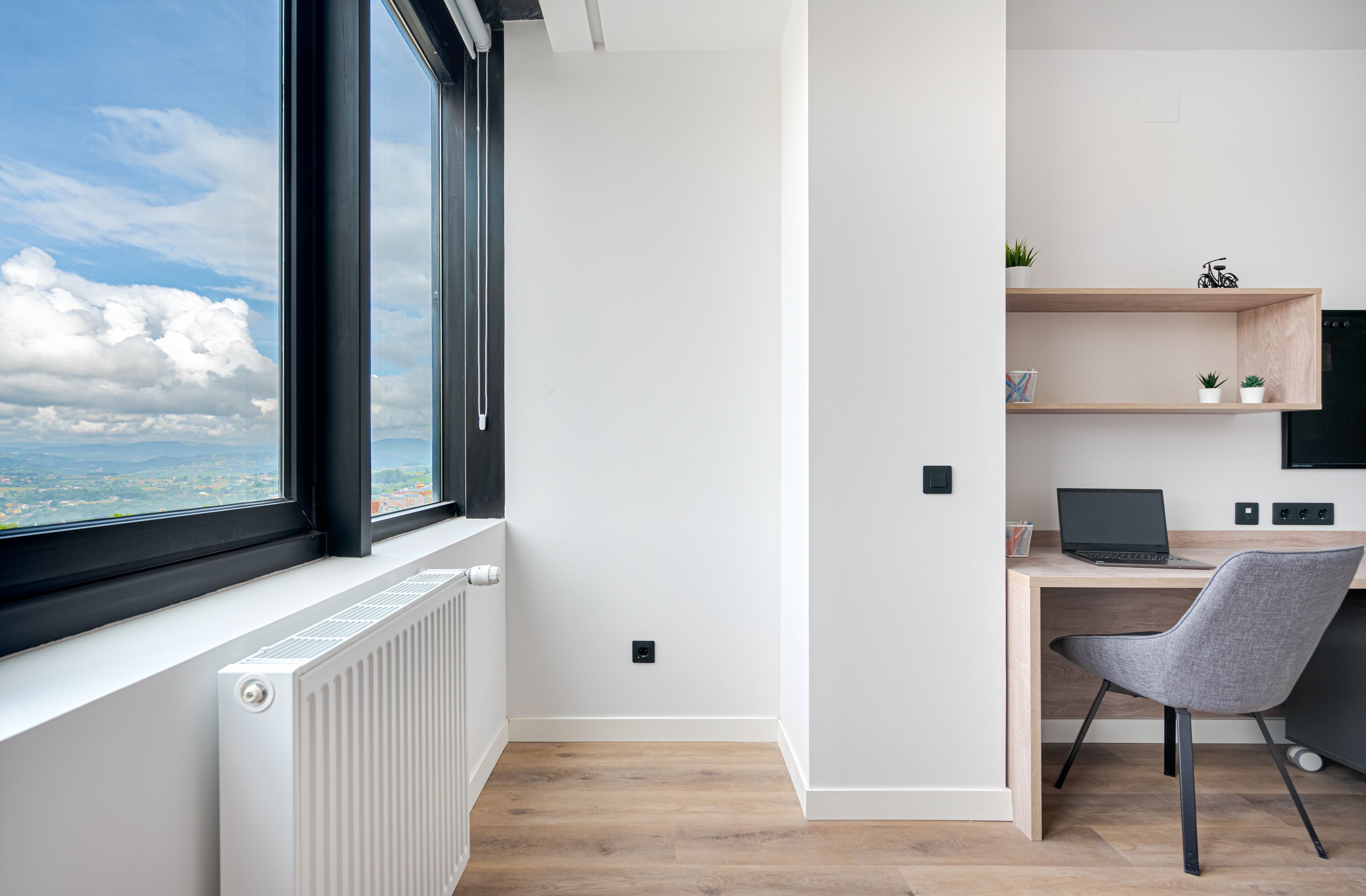 Un espacio de oficina moderno con un ventanal grande, un escritorio, una silla y una estantería con plantas.