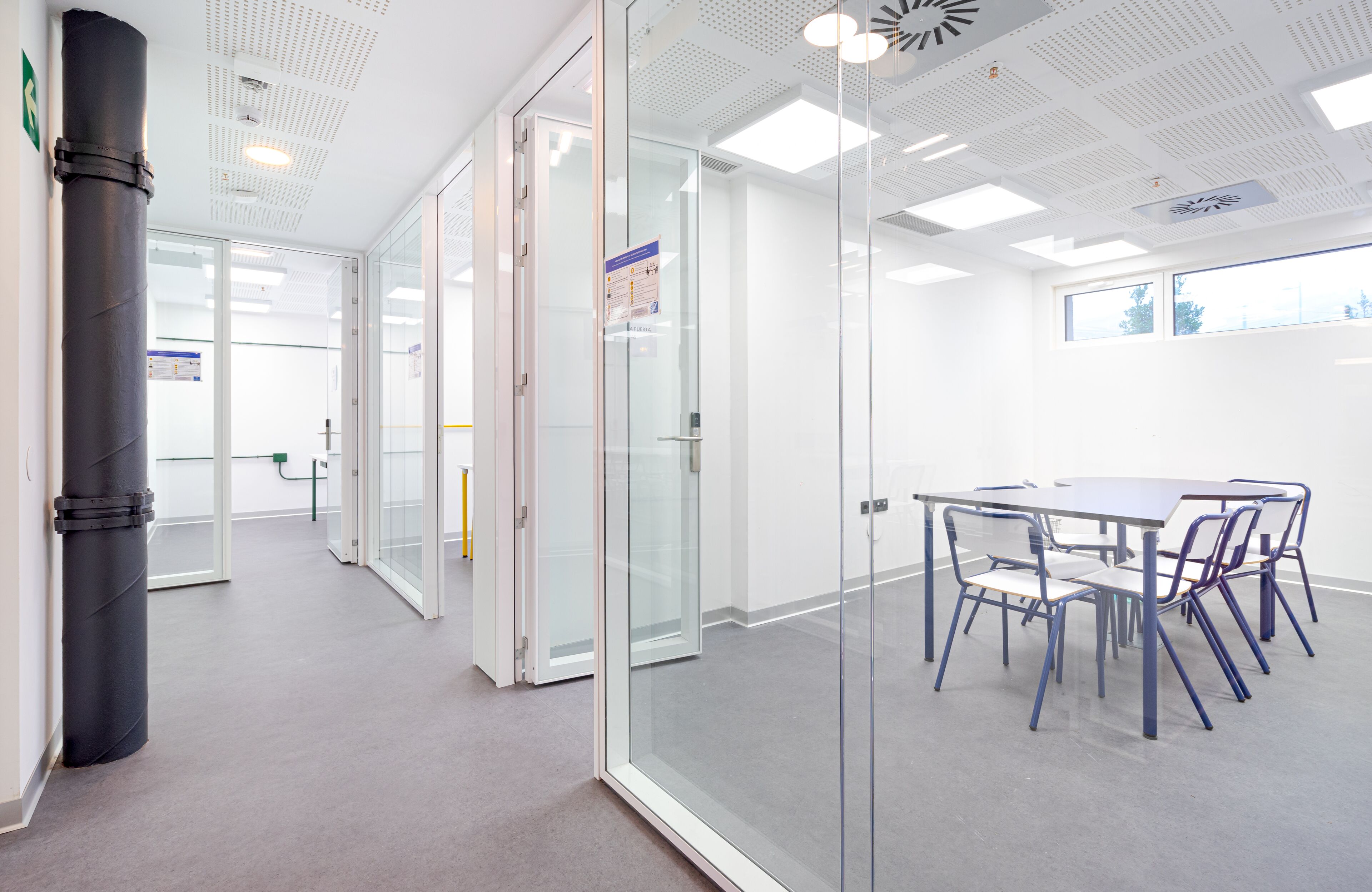 Un espace de bureau moderne avec des murs en verre, une table de réunion entourée de chaises et un plafond doté d’un éclairage encastré.