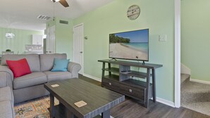 A living room with a gray sofa, a wooden coffee table, and a TV on a wooden stand. - Adorable Townhome with Water Views (Jacksonville)