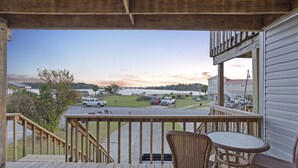 A wooden deck with wicker chairs and a table, overlooking a parking lot and houses. - Adorable Townhome with Water Views (Jacksonville)