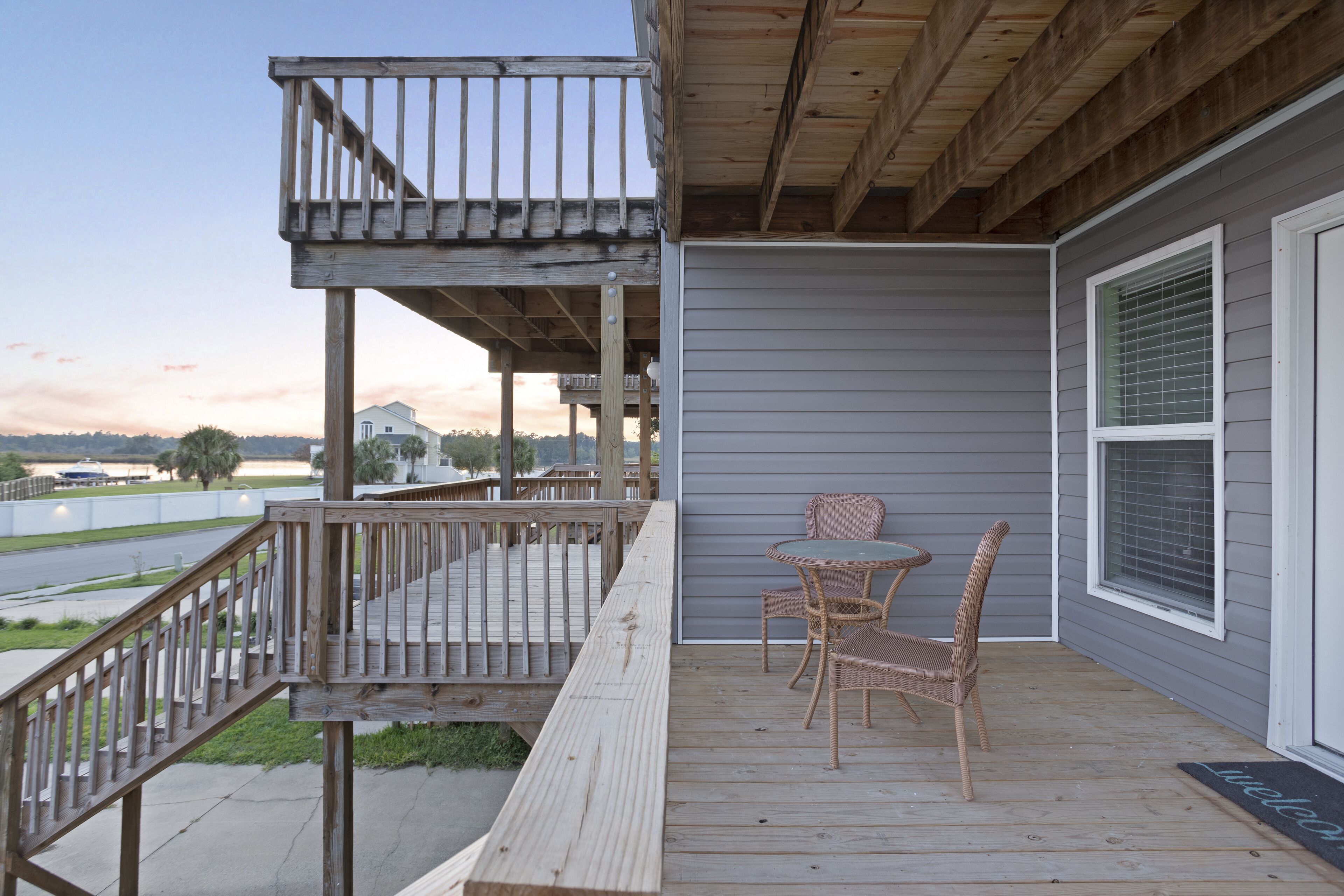 A wooden deck with a railing, a table with chairs, and a welcome mat.