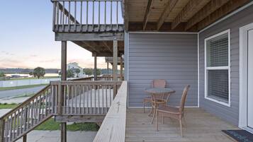 A wooden deck with a railing, a table with chairs, and a welcome mat.