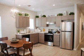 Una cocina moderna con armarios de madera clara, electrodomésticos de acero inoxidable y un comedor con mesa y sillas de madera.