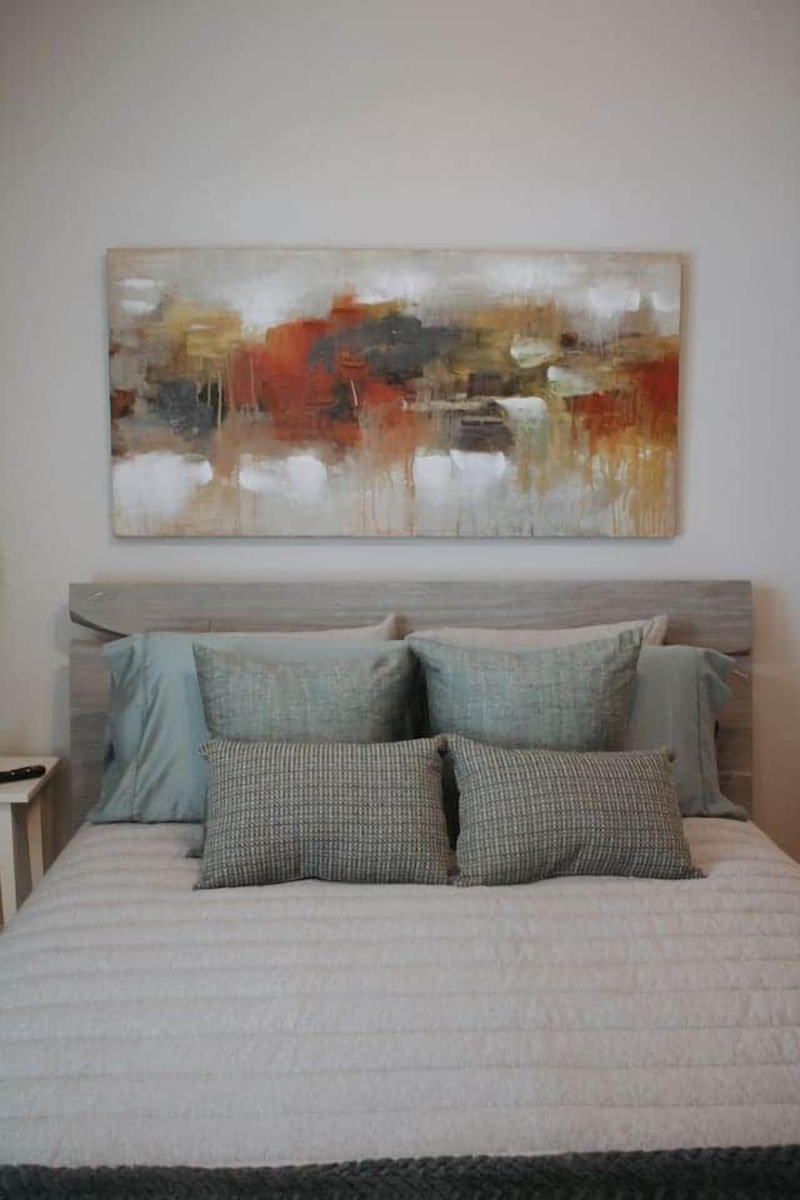 Un dormitorio con cama, almohadas y un cuadro abstracto grande en la pared.