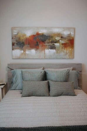 Une chambre à coucher avec un lit, des oreillers et un grand tableau abstrait accroché au mur.