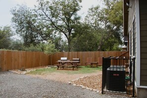 Un patio trasero con cerco de madera, mesa de picnic y parrilla.