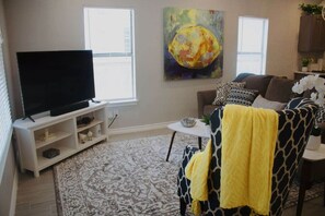 A living room with a flat-screen TV on a white stand, a patterned rug, a giraffe-patterned chair, and a painting on the wall. - Downtown Duplex-San Antonio Unit #1 (San Antonio)