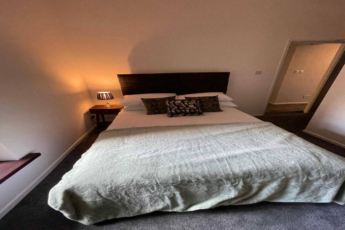 A neatly made bed with a white duvet and two decorative pillows, a bedside lamp, and a dark headboard in a hotel room.