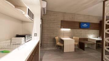 Cocina compacta con microondas, tostadora y lavamanos. Hay un comedor con mesa y sillas. Se ve un letrero de 'MICROTEL by Wyndham' en la pared.