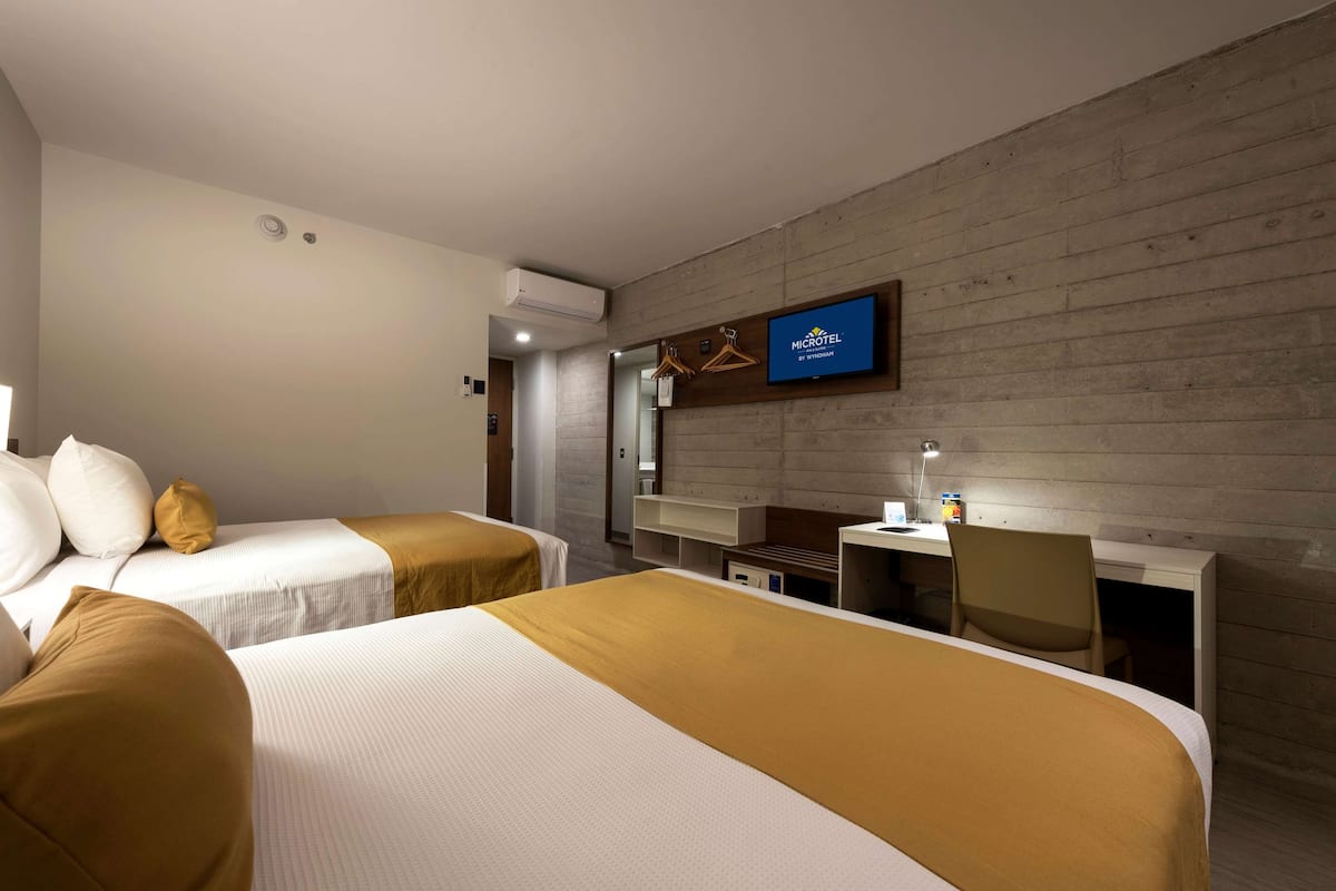 A hotel room with two beds, a desk, and a television.