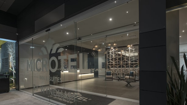 A modern hotel entrance with glass doors, a reception desk, and a patterned interior design. - Microtel Inn & Suites by Wyndham Guadalajara Sur (Tlajomulco de Zúñiga)