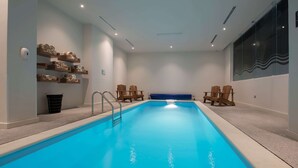 A modern indoor swimming pool with clear blue water, wooden chairs, and a blue bench. - Microtel Inn & Suites by Wyndham Guadalajara Sur (Tlajomulco de Zúñiga)