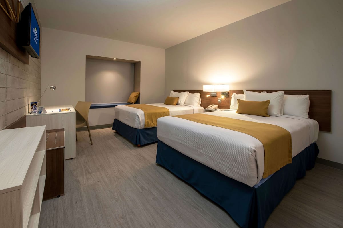 A hotel room with two beds, a desk, and a television.