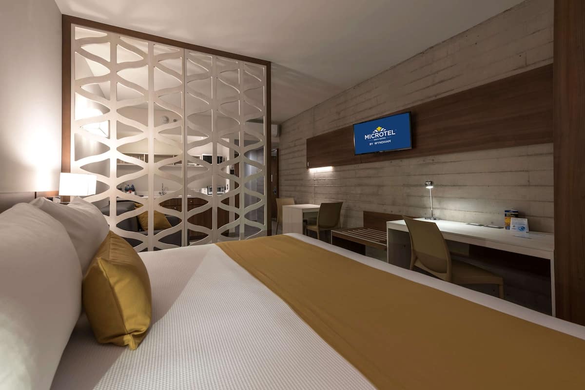 A hotel room with a bed, a desk, and a TV mounted on the wall.