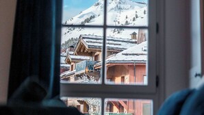 A room with a large window overlooking a snowy mountain and a village.
