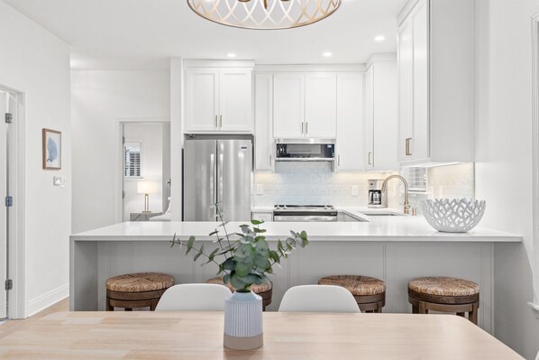 A modern kitchen with white cabinetry, stainless steel appliances, and a central island with stools.