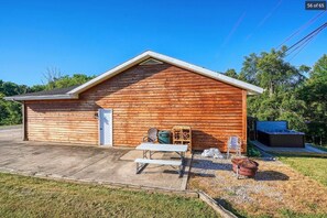 Una cabaña de madera con entrada de hormigón, una mesa de picnic, un jacuzzi y una fogata.