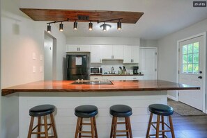 Una cocina moderna con armarios blancos, una encimera de madera y una zona con taburetes de bar.