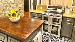 Une cuisine avec un mur en pierre, une table en bois, un vase rempli de tournesols, une cuisinière et un dosseret carrelé.