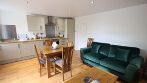 A modern kitchen with wooden cabinets, a dining table with chairs, and a green sofa in a living area. - Charming Flat With Private Patio in Clifton (Bristol)