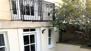 A courtyard with a staircase leading to a balcony, a table with chairs, and a brick wall. - Charming Flat With Private Patio in Clifton (Bristol)
