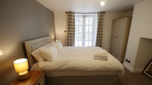 A neatly made bed with white linens, a bedside lamp, and a wardrobe in a bedroom with a window and curtains. - Charming Flat With Private Patio in Clifton (Bristol)