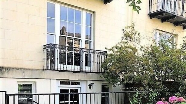 A two-story building with a balcony, a small garden area with pink flowers, and a metal fence. - Charming Flat With Private Patio in Clifton (Bristol)