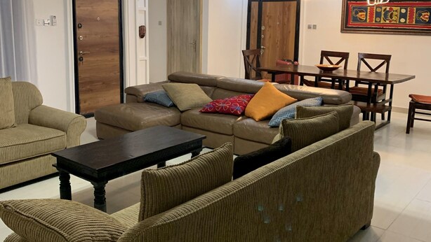 A living room with a sofa set, a dining table with chairs, and a hanging light fixture.