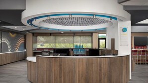 A modern hotel reception area with a curved wooden reception desk, a large window with a view of greenery, and a blue and white ceiling design. - Tru by Hilton San Antonio North (San Antonio)