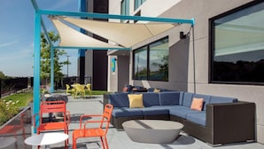 An outdoor seating area with a blue sofa, orange chairs, and a round table. - Tru by Hilton San Antonio North (San Antonio)