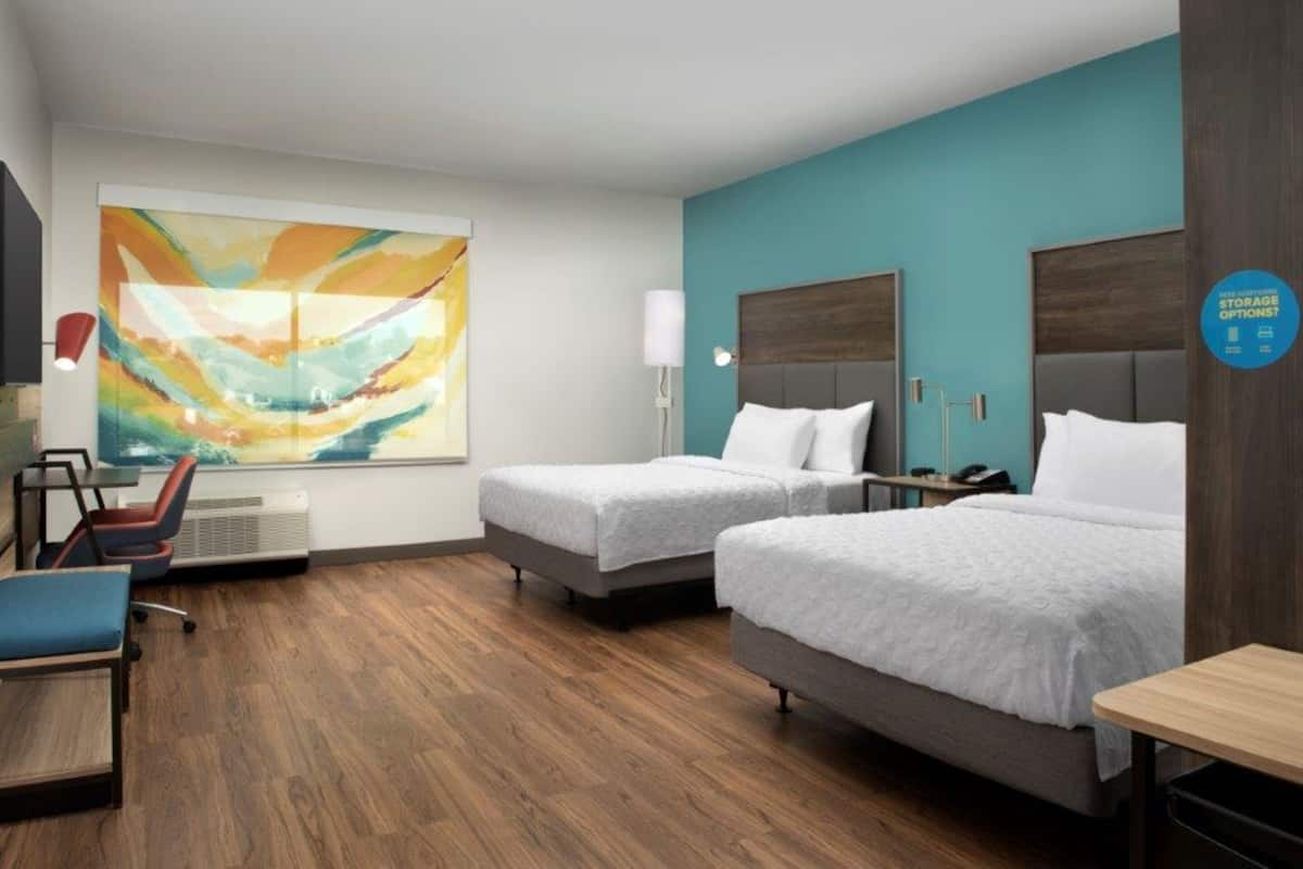 A hotel room with two beds, a desk, a chair, and a large abstract painting on the wall.