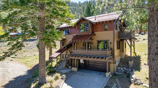 Eine zweistöckige Holzhütte mit Veranda, Garage und kleiner Terrasse.