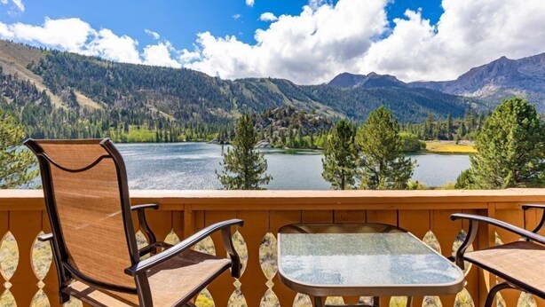 Un balcon avec deux chaises et une table, donnant sur un lac et des montagnes.