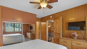 Ein Schlafzimmer mit Bett, Holzschrank, Deckenventilator, Fernseher und Fenster.