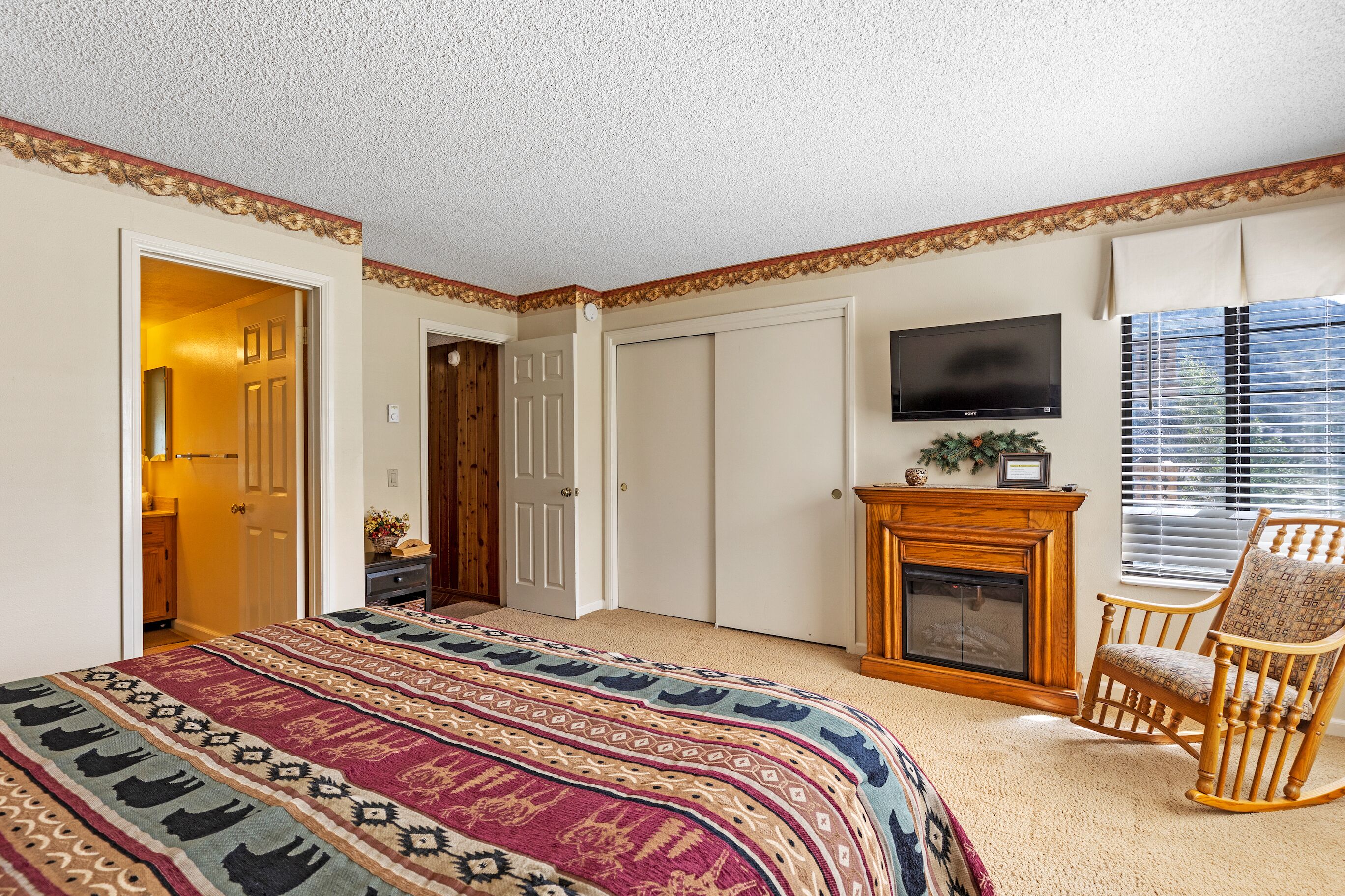 A bedroom with a large bed, a fireplace, a television, and a rocking chair.