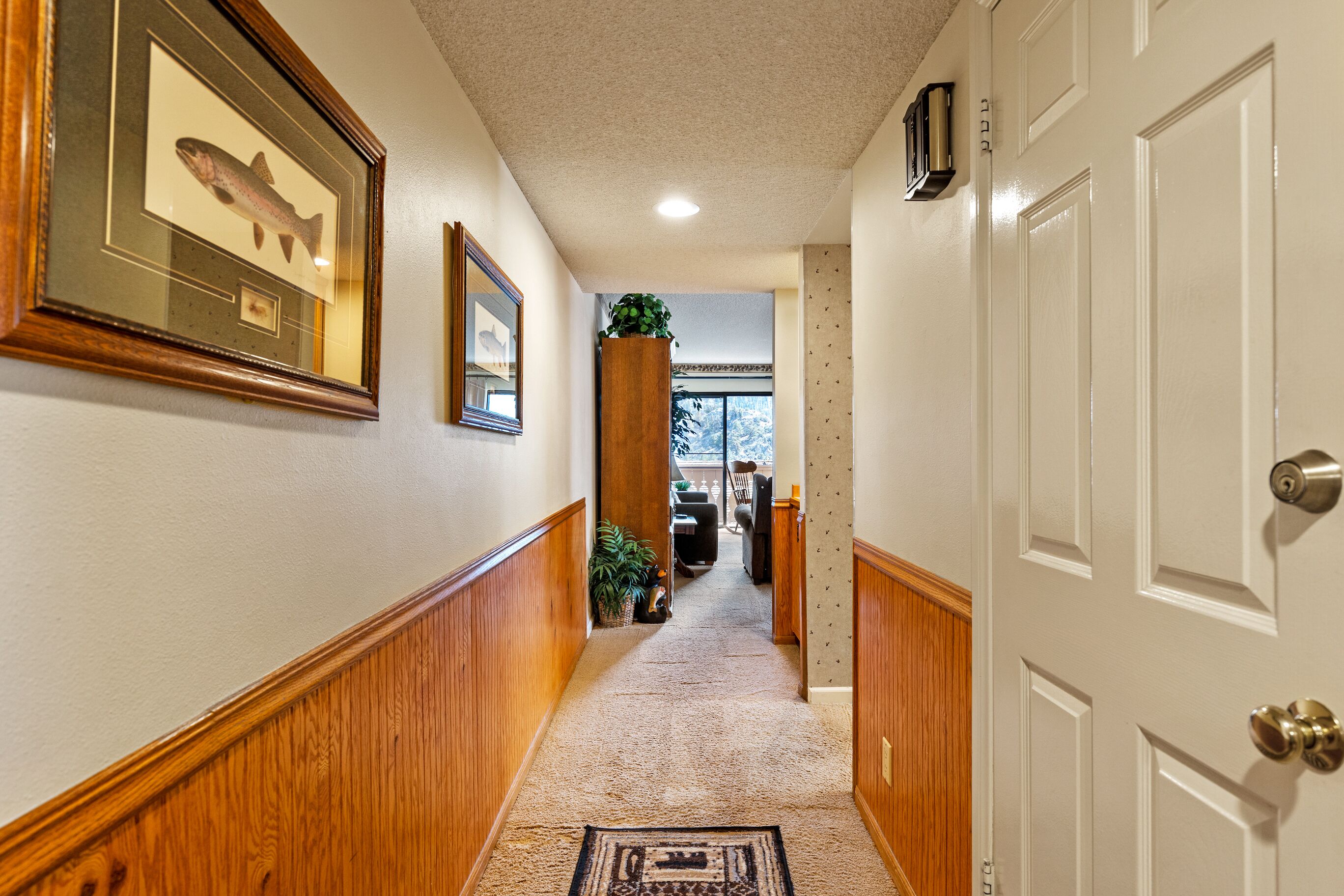 A hallway with wooden paneling, a framed fish picture, a potted plant, and a door with a keyhole.